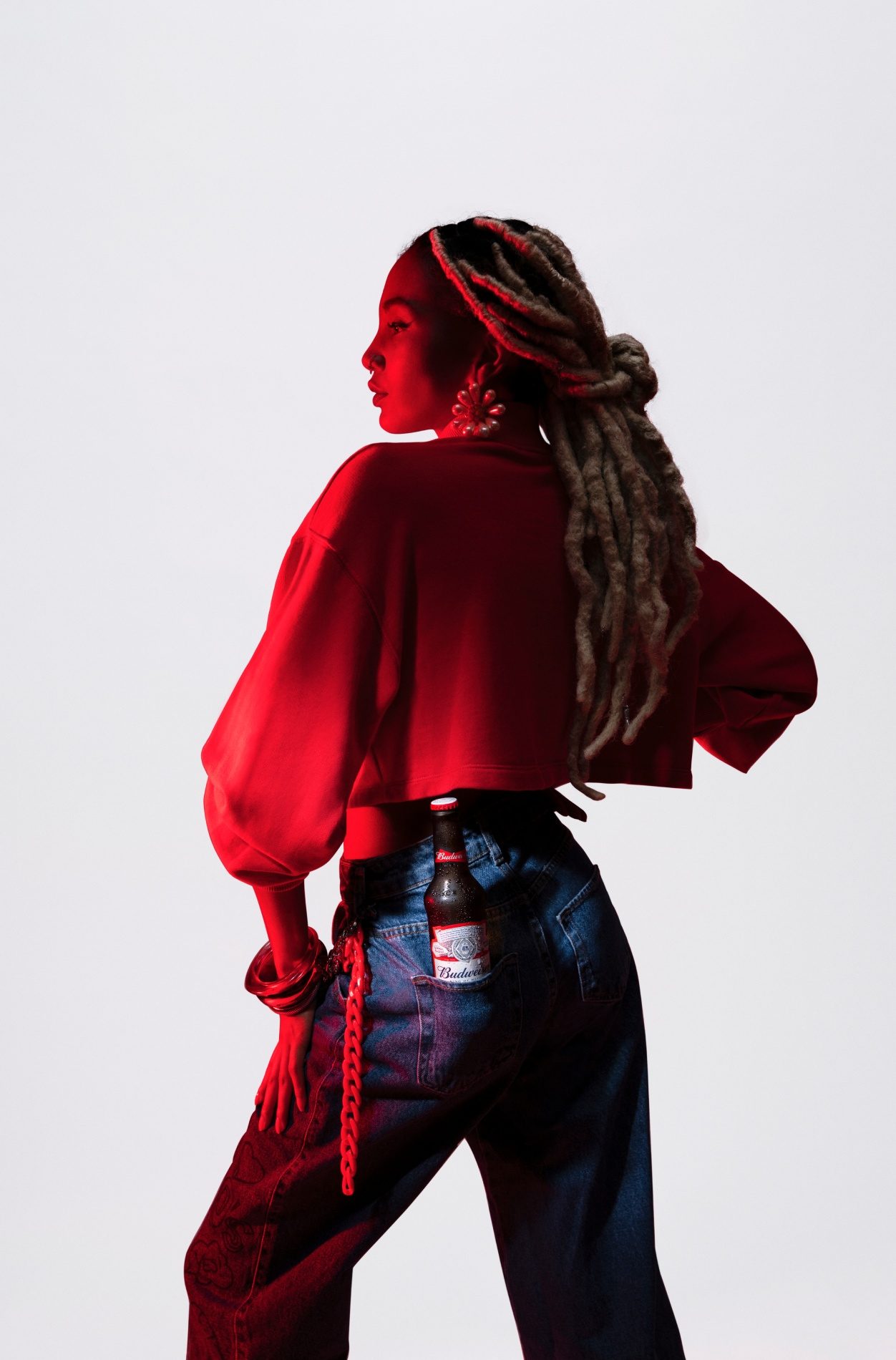 Mulher de costas, de moletom vermelho, com uma garrafa de Budweiser no bolso da calça