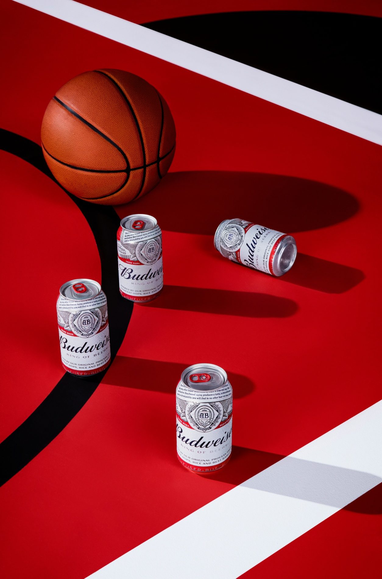 Bola de basquete e latas de Budweiser sobre o piso vermelho de uma quadra