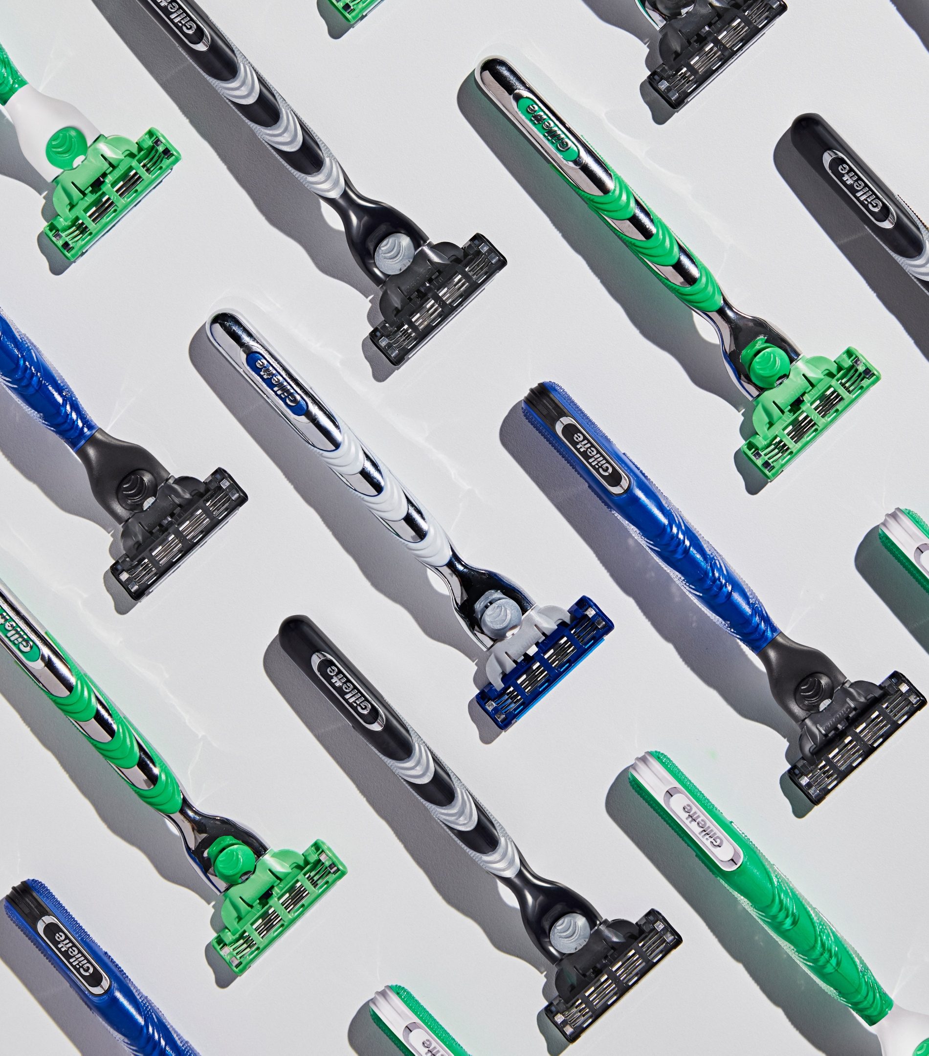 Aparelhos Gillette verdes, azuis e pretos alinhados na diagonal sobre fundo branco