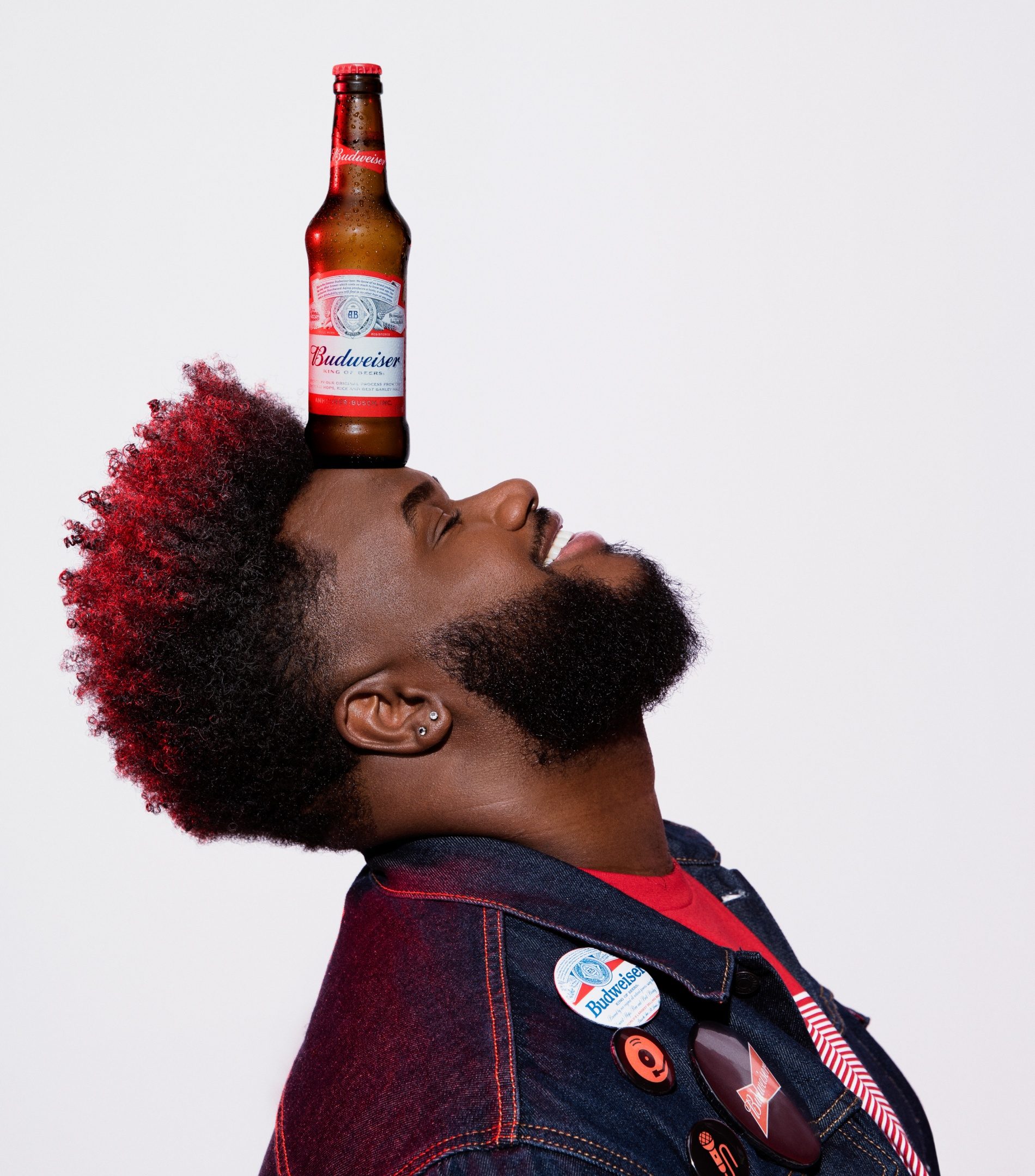 Homem de cabelo vermelho equilibrando uma garrafa de Budweiser na testa