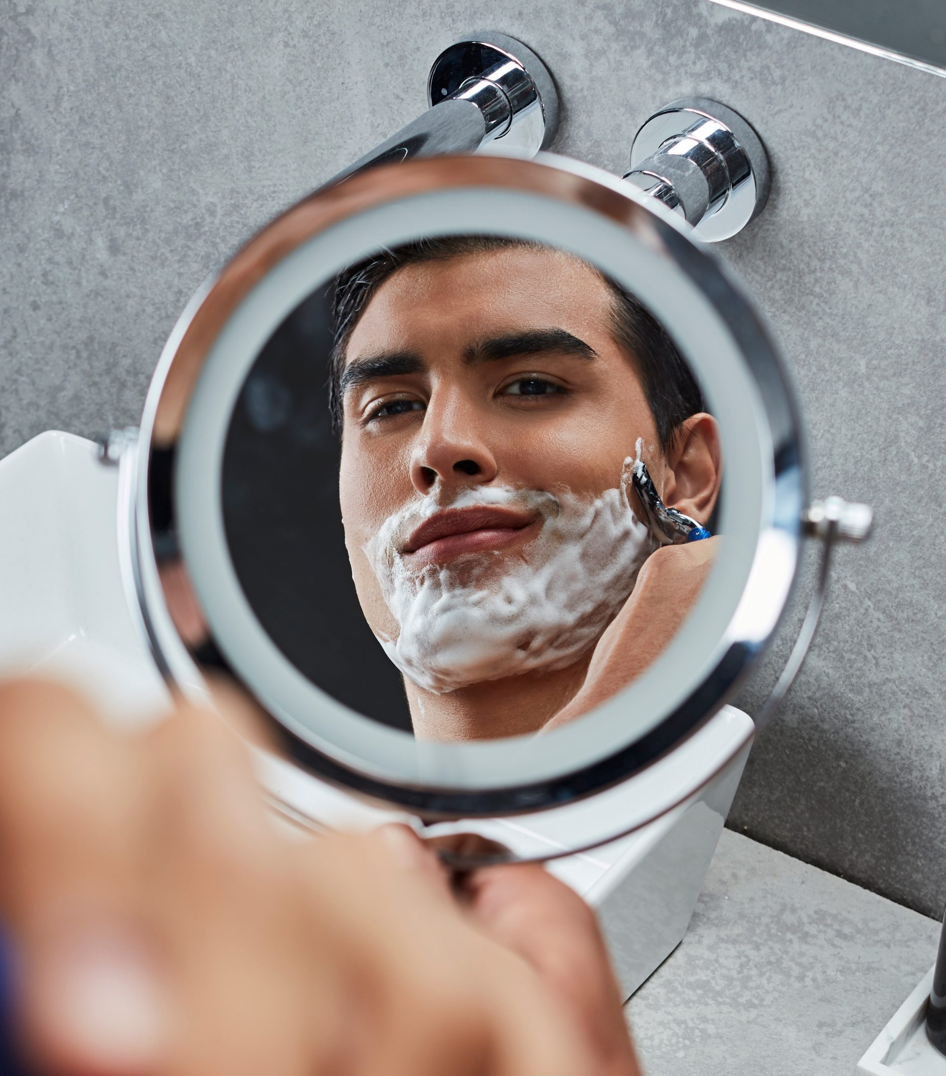 Rosto de um homem com espuma de barbear refletido num espelho redondo