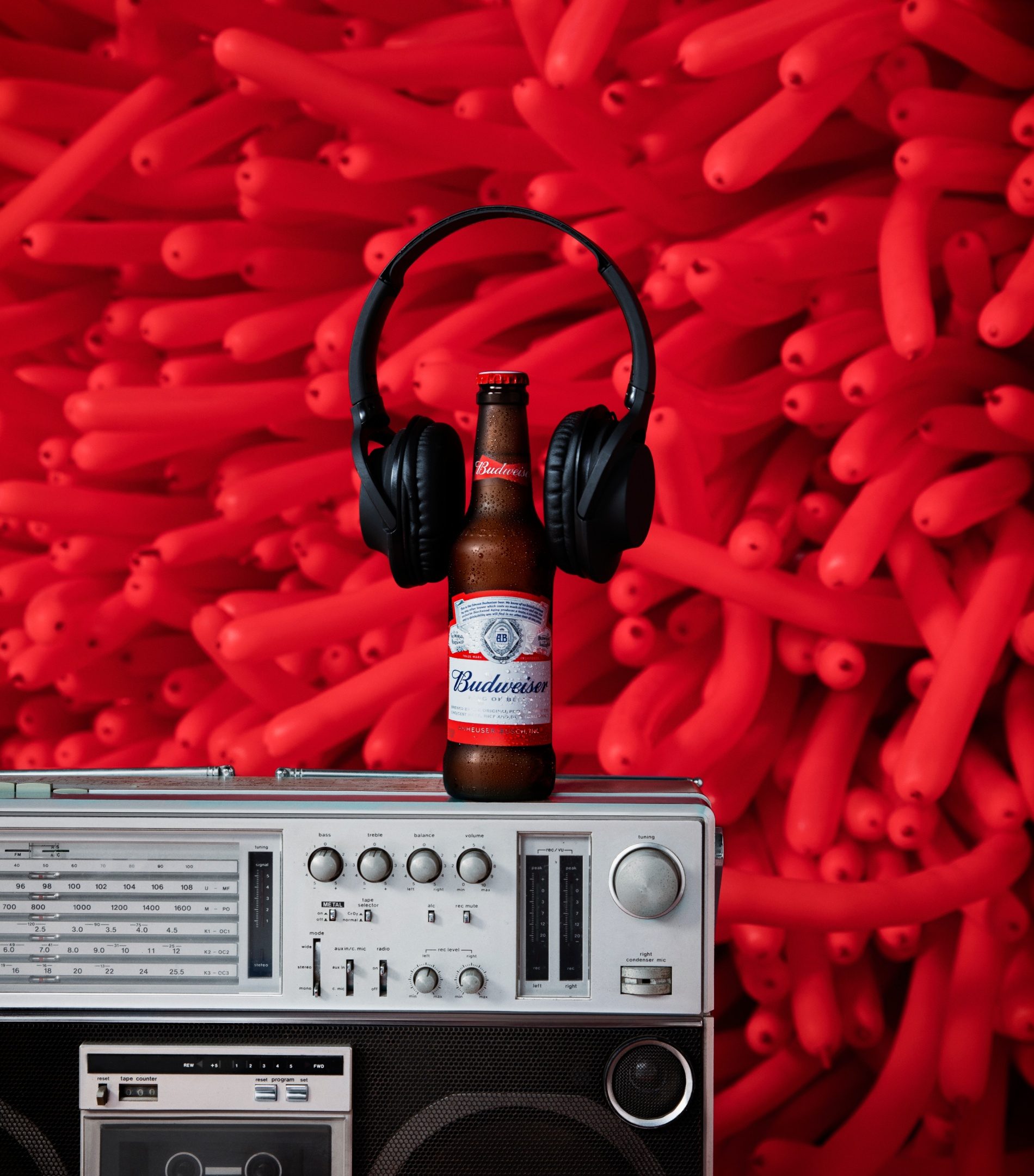 Garrafa de Budweiser com fones de ouvido sobre uma boombox, diante de balões vermelhos