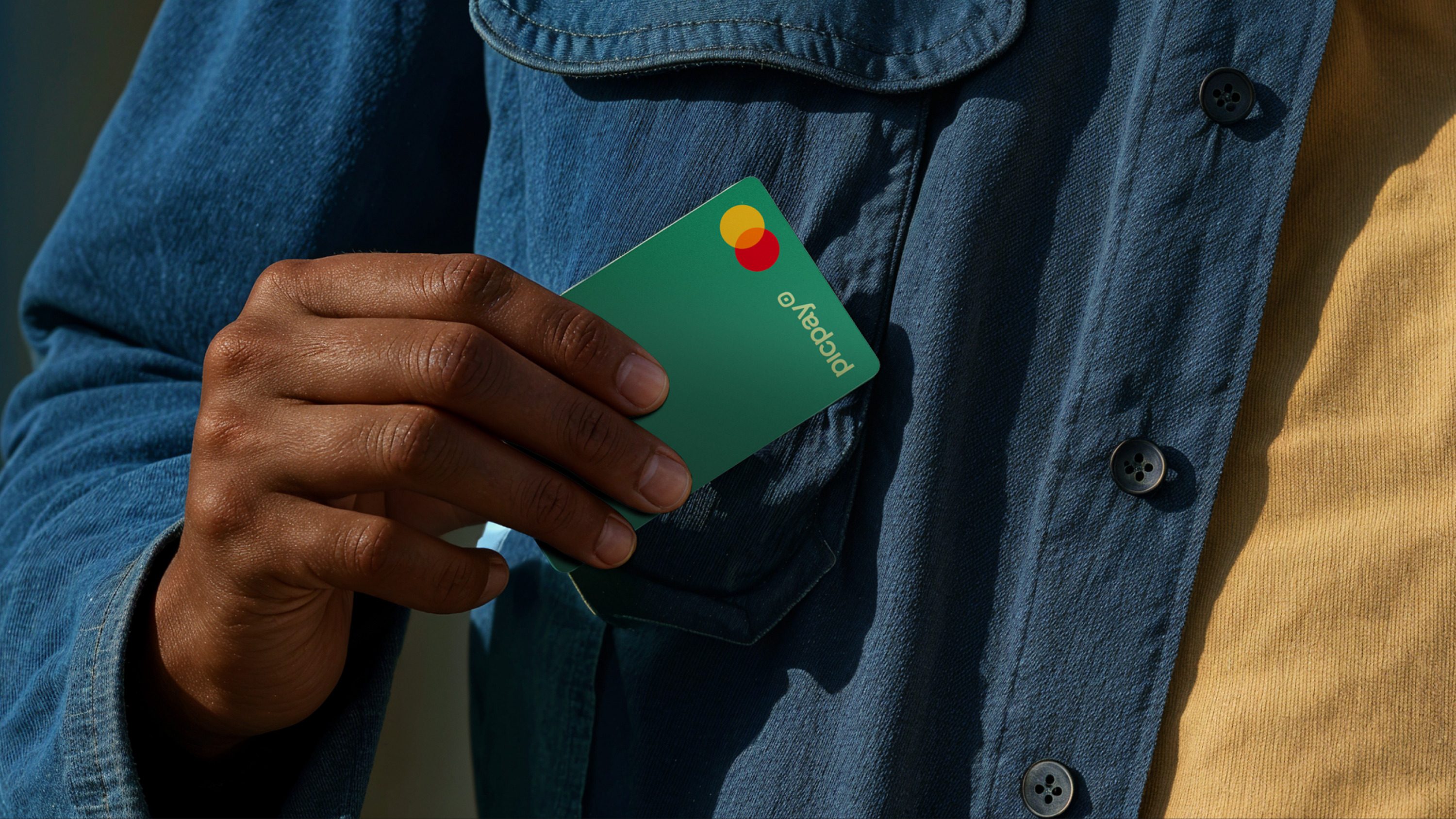 Mão colocando o cartão verde Picpay no bolso de uma camisa jeans