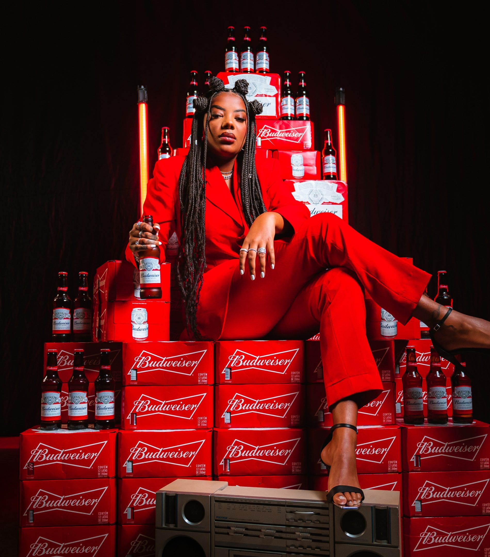 Ludmilla de terno vermelho sentada num trono de caixas e garrafas de Budweiser