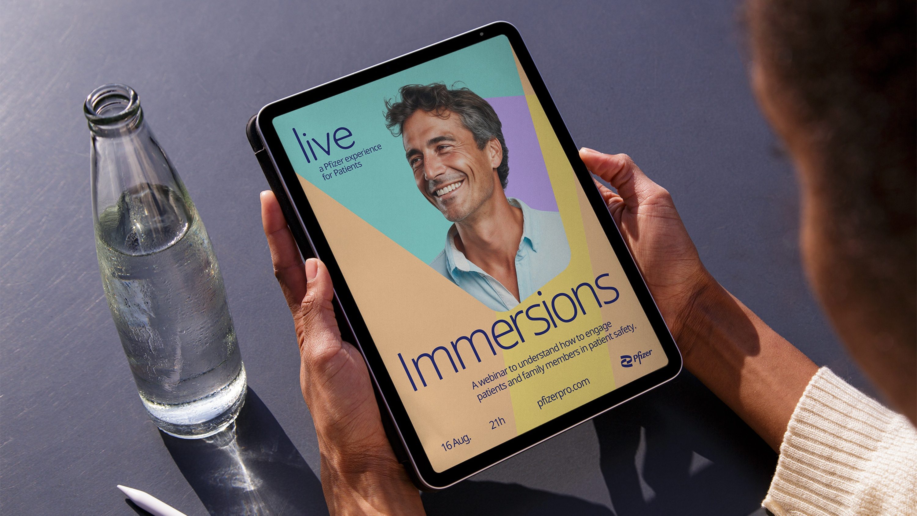 Mãos segurando um tablet com o cartaz de Immersions, um webinar para pacientes