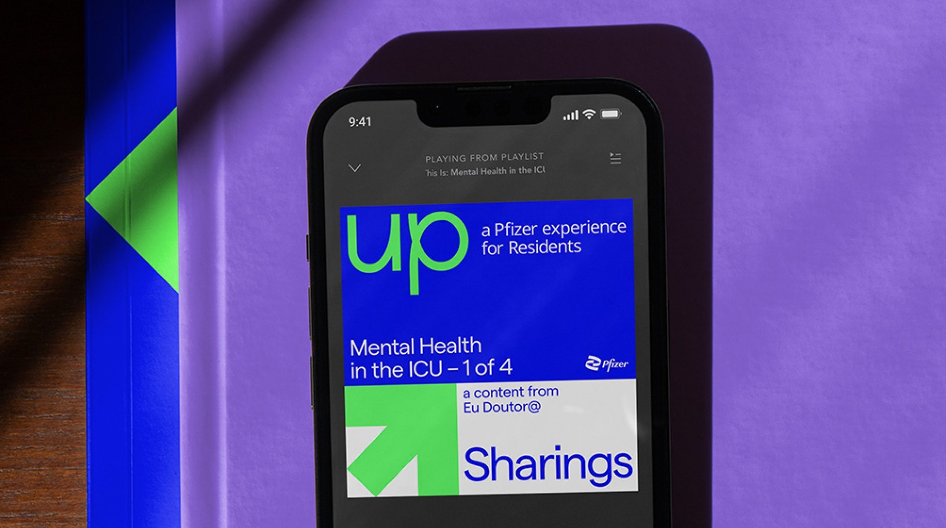 Celular com o podcast Sharings do Up, sobre um caderno roxo